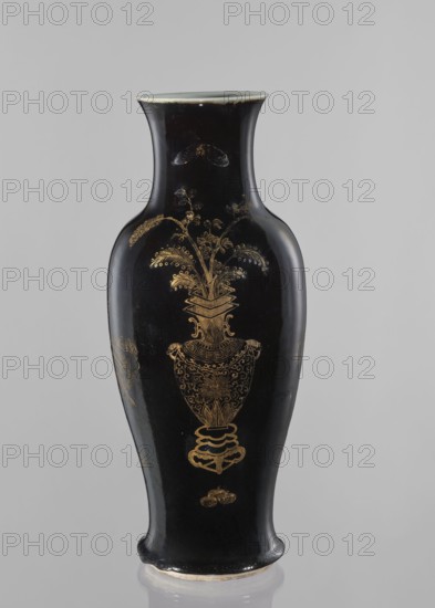 Vase, figural decorations, Chinese, Qing style, figural scenes, ceramics, scenes with a landscape background, gilding, Qing 1644–1911. Elongated vase with a wide neck. Decoration painted with gold on a black background. 19th century, China. Vessel. Height 43.7 cm; diameter 18 cm., A tall, narrow ceramic vase with a flared rim and slightly curved body, finished in glossy black with gold decorative motifs; the central gold design shows an ornate vase or urn filled with stylized leafy stems and fronds, with additional small decorative gold elements above and below; the rim edge and the base show lighter, off-white or pale beige areas where the glaze is thinner, and the overall colors visible are black, gold, and off-white.