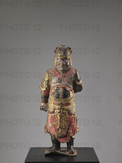 Lokapala — Guardian of the World. Unknown sculptor. Chinese Buddhism. Figurine of a warrior, full sculpture in polychrome red, brown, black. Qing dynasty 1644–1911, 19th century . China. Sculpture, height 72.5 cm., A standing carved figure wearing ornate armor and a helmet, painted in red, black, and gold, displayed on a dark base against a neutral gray background; the figure has a stern facial expression, a rounded belly, a draped skirt with decorative patterns, raised arm and clenched hand, detailed gold embellishments on the chest, waist, shoulders, and helmet, and visible wear and patina on the painted surfaces.
