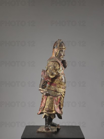 Lokapala Guardian of the World, unknown sculptor; Chinese Buddhism; figurine of a warrior; Qing dynasty 1644–1911; full sculpture in polychrome red, brown, black; 19th century, China; height 72.5 cm., A painted and gilded figure of a standing warrior shown in profile facing right, wearing an ornate helmet and layered armor with decorative embossed details, a flowing skirt-like lower garment, and boots; the sculpture displays visible colors including gold, red, black, and touches of green, with worn and darker areas where paint has aged, and it is mounted on a dark base against a neutral gray background.