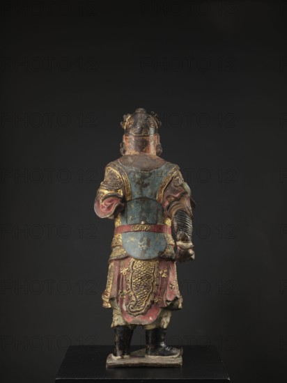 Lokapala Guardian of the World, unknown sculptor; Chinese; Chinese Buddhism; figurine of a warrior; Qing dynasty 1644–1911; polychrome full sculpture in red, brown, and black; 19th century ; China; height 72.5 cm., A painted statue viewed from behind showing a robed figure standing on a rectangular base against a dark background, with visible colors including blue, red, gold, black, green, and brown; the figure wears layered garments with ornate decorative patterns and raised relief details, a belted waist, a lower robe with textured scale-like motifs, and sleeves with folds, and has a helmet or headdress with sculpted elements and worn paint; the boots are black and the base shows scuffed paint.