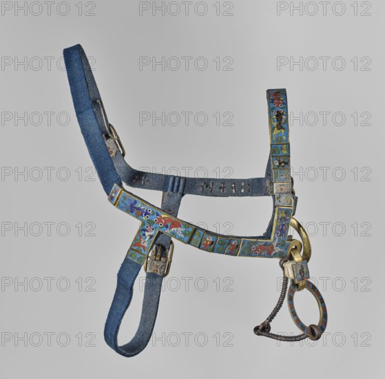 Bit, Chinese art, Chinese culture, Qing 1644–1911, cloisonné enamel, horses riding equipment, riding equipment, fish, plant ornament. Made of leather ribbon and bronze decorated with cellular enamel on copper colorful, on a blue background. 18th century, China. Horse tack element. Height 20.0 cm, width 7.0 cm., A decorative strap or harness made of blue fabric with metal buckles and rings, featuring a series of rectangular metal panels decorated with colorful enamel designs in blue, red, green, white, and gold; the panels show stylized floral and fish-like motifs in repeated patterns, and one curved metal ring hangs from a braided dark metal chain attached to a larger gold-toned ring, with visible wear on the fabric and metal components.