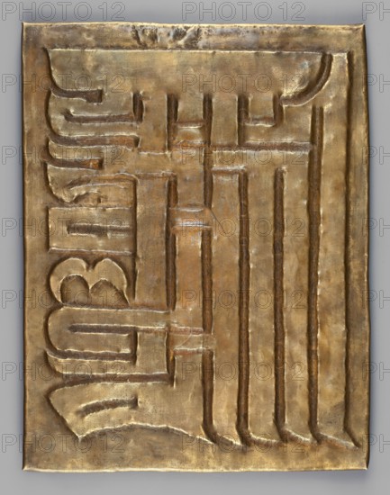 Garuda surrounded by other Buddhist deities; inscriptions; snakes; Kalachakra symbol. Sculpture plaque, height 34.6 cm, width 28 cm. Himalayan/Tibetan Buddhist art; 18th–19th century; possibly Tibet or Mongolia., A rectangular metallic panel with a raised, embossed surface showing an interlocking geometric pattern, rendered in shades of gold with areas of darker bronze and subtle greenish patina; the panel has a slightly irregular edge and visible small dents and creases, with the embossed channels forming rounded and straight grooves that create a repeating vertical and horizontal motif across the surface, and the overall appearance is metallic and reflective with warm golden, brown, and faint green tones.