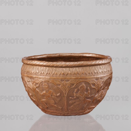 Bowl, repossession Krakow — Vishnu, avatars, turtles, plant ornaments, geometric ornaments, lions, fish, wild boars, flood, Hinduism, trees. Figures of the god Vishnu placed in arcade poses. At the top and bottom an ornament of stylized palm leaves. 19th century, India. Vessel; height 11.5 cm, diameter 18.1 cm., A rounded decorative bowl with a warm coppery brown color and a slightly metallic sheen sits against a pale gray background; the bowl has a raised rim with a braided pattern and a band of textured leaf-like motifs beneath it, while the lower body features a repeating series of carved panels showing stylized human figures in dynamic poses framed by arching vegetal designs, all rendered in the same coppery brown tone with subtle highlights and shadows that emphasize the carved details.