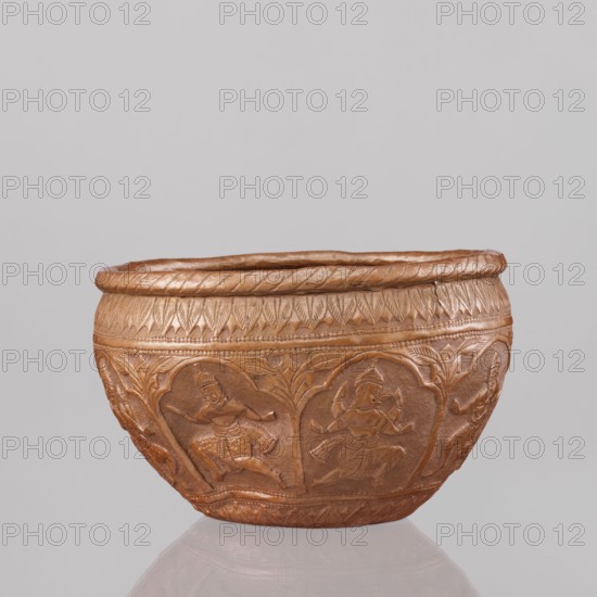 Bowl, 19th century, India; vessel; height 11.5 cm, diameter 18.1 cm. Decoration: figures of the god Vishnu placed in arcade poses; avatars; turtles; lions; fish; wild boars; flood scene; trees; plant ornaments; stylized palm-leaf ornament at top and bottom; geometric ornaments., A rounded decorative bowl made of a brown metallic material sits against a light gray background; the bowl has a textured rim and an embossed exterior with repeating arched panels that contain human figures in dynamic poses, along with patterned borders and leafy motifs; the surface shows variations of brown and copper tones with subtle highlights and shadows.