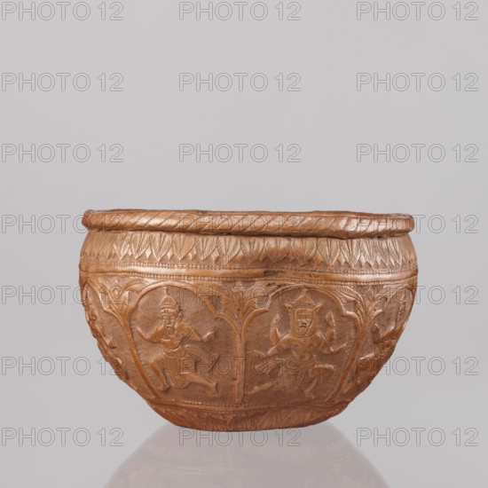 Bowl, 19th century, India. Vessel height 11.5 cm, diameter 18.1 cm. Depicts figures of the god Vishnu placed in arcade poses; Vishnu avatars, turtles; lions, fish, wild boars, flood scenes; trees, plant ornaments, geometric ornaments. At the top and bottom an ornament of stylized palm leaves. Makers unknown., A carved bowl with a rounded shape in a brownish-copper color sits against a plain light gray background; the bowl has a textured rim with a twisted rope-like pattern and a band of carved leaf-like designs below it, while the body features a repeating series of arched panels each containing a carved human figure in dynamic poses, with additional carved foliage and decorative borders around the base, all in similar brown and copper tones.