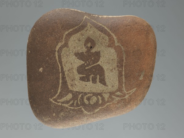 Mani stone, gift, Tibetan Buddhist art, Tibetan culture, Buddhism, mantras, inscriptions, ritual stone, 19th/20th century, Tibet, cult object; weight 1.64 kg, height 14.0 cm, width 15.5 cm, A smooth, rounded stone with a brown surface and a lighter beige design etched or worn into one face, showing an ornate shape with curved outlines and abstract interior forms; the stone displays variations of brown and tan across its surface with a few small lighter flecks, and the background is a uniform muted gray.