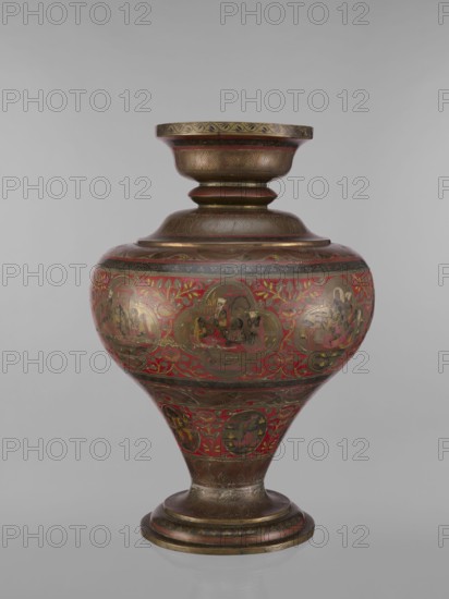 Vase, gift; Indian, 19th century. Vase with a bulging, flattened belly tapering toward the bottom; wide spout and round foot. Polychrome in red, pink, yellow, white and black. Subject motifs: gods Vishnu, Shiva, teachers, fish, plant ornaments, geometric ornaments, ascetics; functions: jug/container. Vessel; height 50.0 cm, diameter 13.0 cm, weight 5.75 kg., A rounded ornamental vessel with a flared rim and pedestal base, decorated with intricate painted scenes and floral motifs; the surface shows a metallic bronze tone with prominent red accents and touches of gold, along with darker brown and black detailing; the body features a band of rounded medallion-shaped scenes set against a red floral background, while the neck and base have carved or painted repeating leaf patterns and linear bands in bronze and brown; the overall shape tapers from a wide midsection to a narrower foot, and the finish appears glossy.