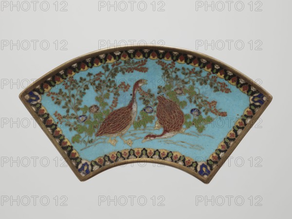 Tray, gift; Japanese; Meiji period 1868–1912; cloisonné enamel; decorated with grass, flowers, and quails; vessel; height 9.5 cm, width 17.3 cm; 19th/20th century., A fan-shaped enamel plaque with a light blue background featuring a decorative border in black, red, white, yellow, green, and blue; inside the border are two stylized birds with brownish-red bodies and gold outlines standing among leafy branches and flowers in green, red, blue, and gold; the plaque has a thin gold-colored rim and rests against a pale gray background.