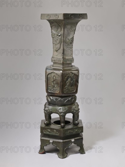 Vase-shaped stove, Chinese art, Chinese culture, unknown provenance; vase-shaped stove decorated with plant ornament, pines, phoenixes, tigers, lotus throne, gourds, dragons, sages, vipers, warriors, lions; associated with Chinese Buddhism, Taoism, and Immortals iconography; Qing dynasty 1644–1911, 19th century, China; height 138 cm, width 42 cm, weight 65.5 kg., A tall sculptural object made of dark greenish bronze with areas of brownish patina stands against a neutral light gray background; its form includes a wide flat top with carved circular motifs, a flared central shaft with raised decorative reliefs and engraved cloudlike patterns, a hexagonal midsection with carved panels depicting human figures in relief, a rounded lotus-shaped collar, and a base formed by a group of curved legs with lionlike faces and ball-shaped feet resting on a stepped plinth that has carved decorative bands and scalloped cutouts.