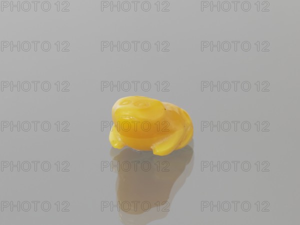 Frog, Chinese, Qing dynasty 1644–1911, 19th century; sculpture/figurine of a frog; materials unspecified; dimensions: height 1.0 cm, width 1.9 cm, depth 1.4 cm., A small, glossy yellow object shaped like a stylized frog sits on a smooth, reflective surface, showing a soft reflection beneath it; the background and surface are shades of light gray, and the yellow object has slightly darker yellow shading and subtle highlights on its rounded forms.