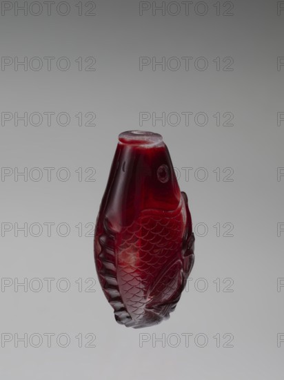 Snuffbox with spoon, red and white stained glass; 18th century, China Qing dynasty, 1644–1911; decorated with carps/fish; vessel/snuffbox; height 7.5 cm, width 4.6 cm., A three-dimensional carved object shaped like a fish in a deep red color with translucent areas, showing carved scales and fins, a rounded top with a flat rim, and a smooth glossy surface set against a neutral gray background with gradations from darker to lighter gray.
