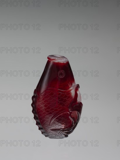 Snuffbox with spoon;, Red and white stained glass snuffbox decorated with bottles and carp fish; Chinese, Qing dynasty 1644–1911, 18th century. Vessel snuffbox. Height 7.5 cm, width 4.6 cm., A translucent carved object shaped like a fish rendered in deep red with areas of darker and lighter red, showing carved scale and fin patterns and a rounded top, photographed against a smooth gray gradient background.