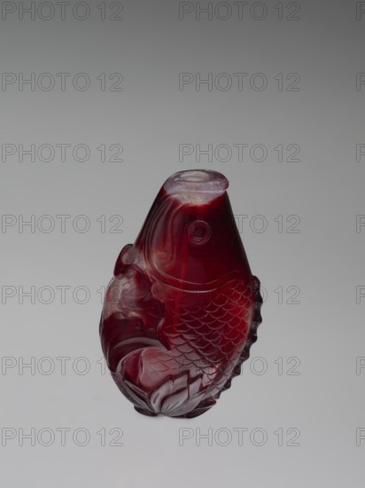 Snuffbox with spoon, red and white stained glass; 18th century, China Qing dynasty, 1644–1911; decorated with carp/fish motifs; vessel/snuffbox; height 7.5 cm, width 4.6 cm., A carved object resembling a fish with textured scales and flowing fins in deep red and burgundy tones, with areas showing darker and lighter variations of red and a few translucent highlights, set against a smooth light gray background.