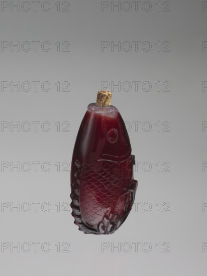 Snuffbox with spoon;, Snuffbox in the shape of a fish with a folded fin, with spoon. Materials: bottles? unclear, Chinese art; Chinese culture; Qing dynasty 1644–1911. Subject: carps, fish. Date: 18th century. Place of origin: China. Function: vessel/snuffbox. Dimensions: height 7.0 cm, width 4.0 cm. Unknown provenance., A carved, translucent deep red object shaped like a fish with textured scale and fin details and a rounded top sealed with a small, light brown cork, set against a smooth gradient gray background with visible shades of pale gray and darker gray.