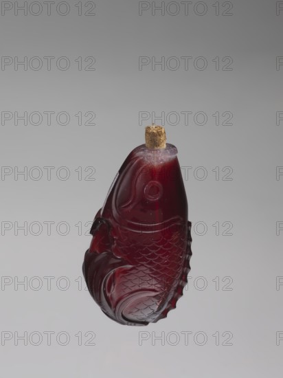 Snuffbox with spoon;, Snuffbox in the shape of a fish with a folded fin, with spoon; materials: bottles? uncertain, Chinese art; culture: Chinese; period: Qing 1644–1911, 18th century; function: vessel/snuffbox. Subject: carps/fish. Dimensions: height 7.0 cm, width 4.0 cm. Provenance: unknown., A carved, fish-shaped object made of translucent deep red material with visible scale and fin patterns, topped with a small cylindrical cork piece; the background is a smooth gradient of light gray to darker gray.