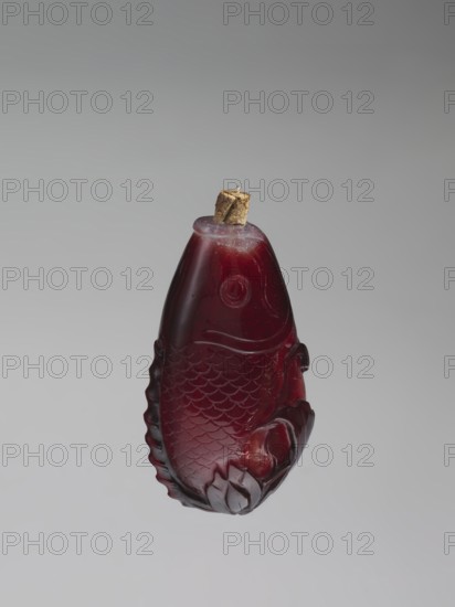 Snuffbox with spoon;, Snuffbox in the shape of a fish with a folded fin, with spoon. Porcelain or ceramic vessel; bottles motif, carps/fish imagery; Chinese art, Qing dynasty 1644–1911, 18th century, China. Height 7.0 cm, width 4.0 cm., A carved object shaped like a fish suspended against a plain background, made of a translucent deep red material with lighter red highlights and small areas of darker red shading; the fish has carved scales, a circular eye, a curved mouth area, and decorative fins, with a small brown cork or stopper set into the top.