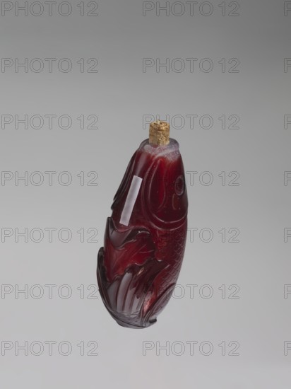 Snuffbox with spoon;, Snuffbox in the shape of a fish with a folded fin, with spoon. Materials: likely bottles? — features carps/fish motif; Chinese art; Chinese, Qing dynasty 1644–1911. 18th century, China. Function: vessel/snuffbox. Dimensions: height 7.0 cm, width 4.0 cm., A carved bottle shaped like a fish made of deep red translucent material with a cork stopper at the top, showing carved scale and fin details and glossy highlights, set against a smooth gradient gray background with shades of light gray and darker gray.