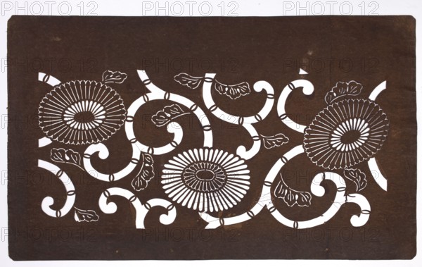 Dyeing stencil katagami with a motif of stylized chrysanthemums and plant tendrils kawari kiku ni karakusa moyô, Meiji 1868–1912, ise-katagami stencil, chuban format, floral ornaments, chrysanthemums, karakusa pattern, 19th/20th century Meiji period, Japan; height 41.3 cm, width 25.0 cm., A rectangular sheet with a dark brown background and white cutaway areas forming a decorative floral design, including a group of three large round flower shapes with radiating petal-like spokes and central oval forms, connected by a network of curving, segmented vine-like bands and several stylized leaf shapes; the white shapes create high contrast against the brown and the sheet shows slight edge wear and a few small scuffs.