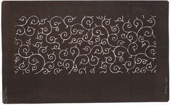Dyeing stencil katagami with a plant twig motif karakusa, Taisho 1912–1926, ise-katagami stencil in chuban format, plant twig karakusa pattern, Japan, stencil; height 40.7 cm, width 25.2 cm, 1912–1926., The image shows a dark brown rectangular surface with a horizontal band of intricate white swirling, curling vine-like patterns across the upper half; the lower portion is mostly plain dark brown. The swirls vary in size and form a dense repeating ornamental design. The edges of the rectangle show a thin white border on two sides, and there are small lighter brown variations and tiny marks on the darker background. The visible colors are dark brown, white, and lighter brown.
