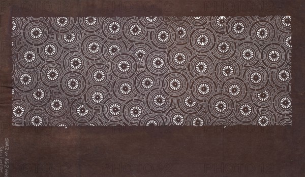 Katagami dyeing stencil with a motif of stylized floral rosettes kawari kamon moyô; ise-katagami stencil, chuban format; geometric and plant patterns; stencil; height 40.6 cm, width 24.1 cm; Japan; 2nd half of the 19th century Edo/Meiji periods., A rectangular area filled with a repeating circular dot pattern sits against a darker background; the patterned area shows concentric rings of small white dots forming circles with starburst-like white centers, and the surrounding background is a deep brown while the dots and starburst centers are white, creating a contrast between white and dark brown.