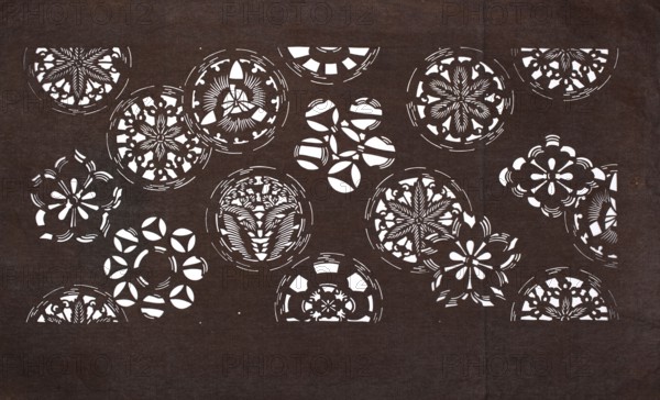 Katagami dyeing stencil with a motif of stylized floral rosettes and cherry blossoms kawari kamon ni sakura moyô, ise-katagami stencil in chuban format, geometric and plant patterns, flowers, sakura iconography, Meiji period, 2nd half of the 19th century 1868–1912, Japan; stencil; height 40.6 cm, width 24.7 cm, A dark brown background with a group of white circular cutout patterns arranged across it, each circle containing floral and geometric designs; several show petal-like shapes, starburst motifs, and radiating line details, while a few circles are partially visible at the edges.
