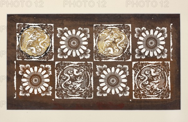Katagami dyeing stencil with a stylised checkered motif with dragons and chrysanthemums ichimatsu ni ryû to kiku moyô, ise-katagami, stencils, chuban format, pattern cut out on the base: a grid of eight squares with alternating flower rosettes and a dragon inscribed in a circle, stencil, 2nd half 19th century Meiji period, Japan, height 39.8 cm, width 24.8 cm., A rectangular artwork with a dark brown background framed by a light beige border shows a grid of decorative square panels arranged in two horizontal rows. Each square contains a white ornate motif, alternating between floral rosette designs and circular dragon-like figures; the dragon-like circles in some squares have metallic gold accents. The floral motifs are stylized with white petal shapes radiating from a central disk, and the dragon-like motifs feature swirling lines and curving forms within white square borders. The overall palette includes dark brown, white, beige, and touches of gold.