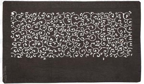 Katagami dyeing stencil cut into a pattern of stylized plant tendrils karakusa; maker, stencil; floral tendril motif; Japanese; 19th–20th century Meiji period, 1868–1912; height 40.7 cm, width 24.4 cm., A rectangular dark background with a lighter ornate cutout area near the top showing a dense, repeating swirling vine pattern with small leaf-like shapes; the cutout area contrasts with the dark surrounding field, and the visible colors are dark brown or black for the background and white or very light cream for the cutout pattern.