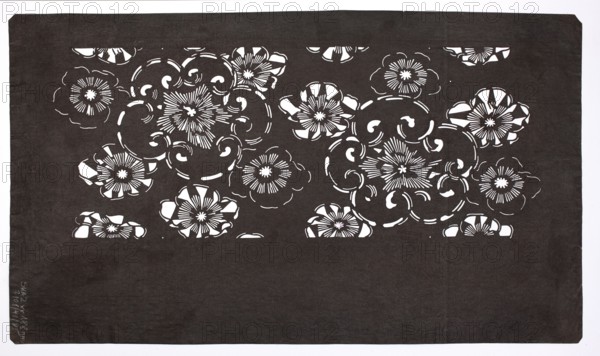 A katagami dyeing stencil cut into a pattern of stylized flower rosettes of various sizes ise-katagami, Japanese, 19th/20th century Meiji period, 1868–1912. Stencil; height 40.5 cm, width 23.2 cm., A rectangular sheet with a dark background and a decorative band across the upper portion featuring a repeating floral cutout pattern, showing a group of stylized flowers and swirling vine-like shapes where the dark surface contrasts with the lighter cutout areas; the visible colors are dark gray or black for the sheet and white for the cutout spaces, with the surrounding border appearing white.