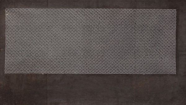 Katagami dyeing stencil; geometric pattern made of a dense grid of small rhombuses, Japanese, Meiji period 1868–1912, ise-katagami stencil, geometric ornaments, 19th–20th century, Japan; height 41.0 cm, width 24.1 cm, A rectangular area filled with a repeating small circular and X-shaped pattern in white sits near the top of a darker rectangular background; the patterned area is framed by a wider dark border with visible texture and subtle worn marks, showing colors of black, dark brown, and hints of rust, while the pattern area contrasts in white against a dark backdrop.