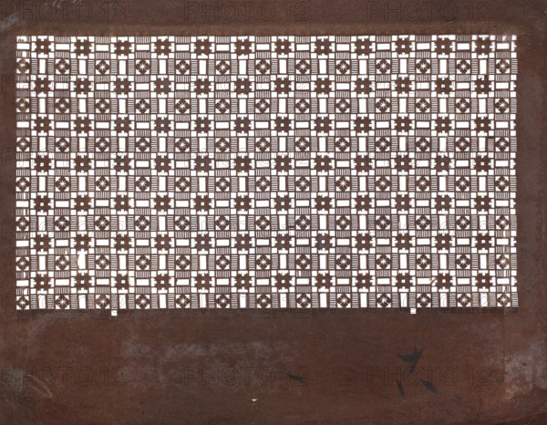Katagami dyeing stencil; pattern with a dense arrangement of ornamental squares and stripes, katagami, stencils, Japanese art, geometric motifs, Japanese, 19th/20th century Meiji period, 1868–1912, Japan, stencil, height 40.1 cm, width 30.6 cm, A rectangular sheet with a dense grid of small square cutouts forming a repeating geometric pattern sits centered against a textured background; the cutouts create alternating motifs of cross-like stars and striped rectangles, revealing bright negative space that contrasts with the darker surface. The background and the sheet are primarily deep brown with variations in tone, showing lighter brown scuffs and worn areas, and there are a few small dark smudges and marks near the lower area of the image.