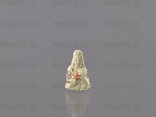 Seated female figure - Guanyin, gift, repossession, female images, Japanese art, ceramics, figurines, Japanese, early 20th century, Japan, sculpture, height 3.7 cm, width 2.4 cm, A small pale figurine with a smooth surface sits against a muted gray background, showing a faint reflection beneath it; the figurine is primarily off-white or cream with painted accents in pink, red, and black, and appears to feature a rounded head and draped clothing with floral-like painted designs.