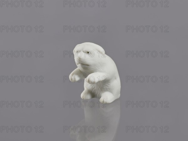 Puppy, unknown ceramicist, gift, Meiji 1868–1912, Japanese art, Japanese culture, ceramics, figurines, animals, dogs, early 20th century Meiji period, Japan, Hirado, sculpture, height 7.0 cm, width 3.6 cm, weight 46.0 g, A small white sculpted figure resembling an animal sits on a smooth reflective surface against a uniform gray background, showing a rounded body, raised front limbs, a textured chest and facial features with subtle indentations; the surface reflection mirrors the figure faintly, and the visible colors are white and gray.