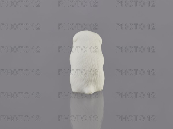 Puppy, unknown ceramicist, gift; Meiji period early 20th century, 1868–1912, Japan, Hirado. Ceramic figurine of a dog sculpture. Height 7.0 cm, width 3.6 cm, weight 46.0 g., A small white sculpted figure viewed from behind sits centered on a smooth reflective surface, showing textured fur-like grooves and rounded ear shapes, with its reflection visible below; the background and surface are uniform gray, and the colors visible are white and gray.