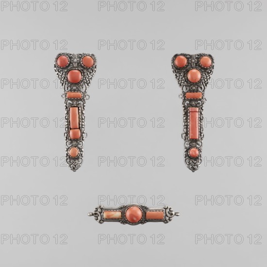 A set of braid ornaments consisting of a clasp and two pendants, late 18th century, Mongolian origin; women's braid ornaments made as jewelry, artistic craftsmanship; dimensions: height 10.0 cm, width 13.0 cm., A group of decorative metal pieces set against a light gray background, each piece featuring ornate silver filigree and a few rounded and elongated coral-colored stones; two vertically oriented matching pieces with heart-shaped tops show intricate silver patterns around coral round and rectangular stones and a few small circular accents, while a separate horizontal bar piece below displays a central round coral stone flanked by rectangular coral stones and decorative silver ends; visible colors include silver, coral, and light gray.