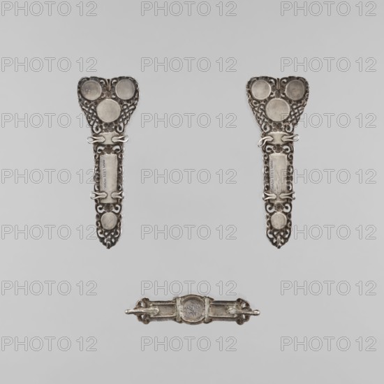 A set of braid ornaments consisting of a clasp and two pendants, craftsman unknown, purchased provenance, clasps, jewelry, artistic craftsmanship, Mongolian art, braid ornaments, women's ornaments, late 18th century, Mongolia, jewelry, height 10.0 cm, width 13.0 cm, A pair of ornate metallic objects with a matching decorative pattern are positioned near the top, each featuring heart-shaped upper sections with circular raised areas and elongated lower sections with openwork scroll details and clasp-like elements; a third smaller metallic piece with a central rounded section and short projecting bars is placed below them. The visible colors are silver, gray, and subtle darker gray tones against a light gray background.