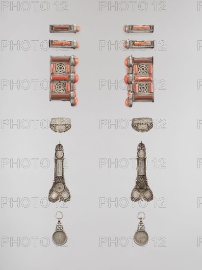 Set of braid ornaments, braid ornaments, artistic crafts, Mongolian jewelry, braids, women's ornaments, 19th–20th century, Mongolia, height 3 cm, width 7.8 cm, A symmetrical arrangement of two vertical sets of ornate metal objects on a pale gray background, each set including a pair of small rectangular items with rounded coral-colored ends, a larger rectangular piece with coral-colored rounded accents and intricate openwork panels, a decorative curved metal plate, a long ornate metal pendant with detailed filigree and geometric shapes, and a round metal medallion hanging from a small ring; visible colors include silver, coral, brown, and pale gray.