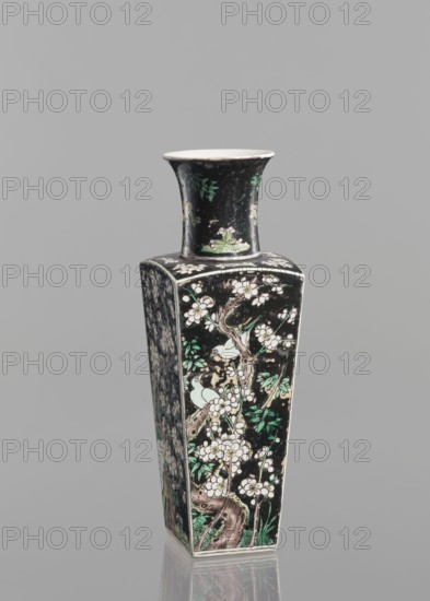 Pair of vases; Chinese; ceramics; colored porcelain in famille noire palette; decorated with birds, plums, and floral motifs; 18th century, China; vessel; height 22.5 cm; ., A tall, square-bodied ceramic vase with a flared neck stands against a plain gray background; the vase has a predominantly black surface decorated with floral and botanical motifs in white, green, and pale pink, showing branches, blossoms, leaves, and a few stylized birds; the neck and panels carry continuous painted patterns with accents of brown and lighter green on the tree trunks and foliage; the base and inner rim are lighter in color, and the vase casts a subtle reflection on the surface below.