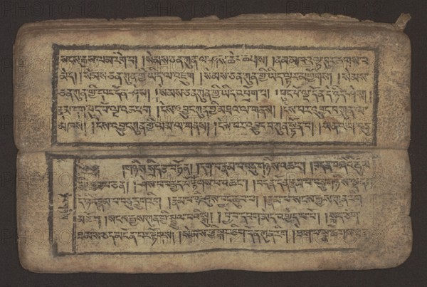 Buddhist text - Commentary on the praise of the names of Manjushri by Ga Rabjampa Kunga Yeshe Tib. 'phags pa 'jam dpal gyi mtshan yang dag par brjod pa zhugs so, unknown creator role, noted, Buddhist art, Tibetan, graphic prints, book in Tibetan pecha style, xylographic print in student script dbu can. 26 folios, recto page numbering, first verso, 2 pages missing. Buddhist commentary on the prayer of praise in honor of the names of the bodhisattva Manjushri Tib. 'jam dpal dbyang by Ga Rabjampa Kunga Yeshe Tib. sga rab 'byams pa kun dga' ye shes. Original text from the 15th century; this copy 19th century, Tibet. Graphics; width 24.6 cm, height 8.0 cm., An open weathered manuscript page lies flat against a dark background, showing two rectangular text blocks framed by thick dark borders; the page surface is aged beige with mottled brown and tan discoloration and darker brown edges, and the ink used for the script and borders appears black to dark brown; the paper has rounded corners and...