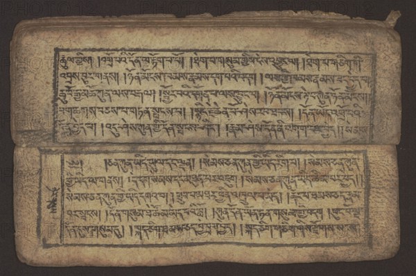 Buddhist text — Commentary on the praise of the names of Manjushri by Ga Rabjampa Kunga Yeshe Tib. 'phags pa 'jam dpal gyi mtshan yang dag par brjod pa zhugs so. Author: Ga Rabjampa Kunga Yeshe Tib. sga rab 'byams pa kun dga' ye shes. Book in Tibetan pecha style, xylographic print in student script dbu can. 26 folios, recto page numbering, first verso, 2 pages missing. Buddhist commentary on the prayer of praise in honor of the names of the bodhisattva Manjushri Tib. 'jam dpal dbyang. Original text from the 15th century; this object dated 19th century, Tibet. Graphics; width 24.6 cm, height 8.0 cm., A worn rectangular object with a faded beige surface bordered by a dark background, showing two horizontal panels separated by a fold. Each panel is framed by a thin dark rectangular border and filled with dense dark markings arranged in horizontal lines. The material appears creased and aged with darker smudges and stains, especially along the edges and fold. The top edge is slightly torn ...