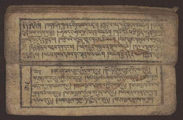 Buddhist text - Commentary on the praise of the names of Manjushri by Ga Rabjampa Kunga Yeshe Tib. 'phags pa 'jam dpal gyi mtshan yang dag par brjod pa zhugs so, Buddhist art, Tibetan; graphic prints; book in Tibetan pecha style; xylographic print in student script dbu can. 26 folios, recto page numbering, first verso, 2 pages missing. Buddhist commentary on the prayer of praise in honor of the names of the bodhisattva Manjushri Tib. 'jam dpal dbyang by Ga Rabjampa Kunga Yeshe Tib. sga rab 'byams pa kun dga' ye shes. Original text from the 15th century; object dated 19th century, Tibet. Graphics; width 24.6 cm, height 8.0 cm., A rectangular, aged manuscript page with a textured beige background and visible wear around the edges, containing two horizontal blocks of dark calligraphic script framed by thin black rectangular borders; the top block sits near the upper edge and the bottom block is separated by a fold or crease across the center, with darker brown stains and smudges scattered...