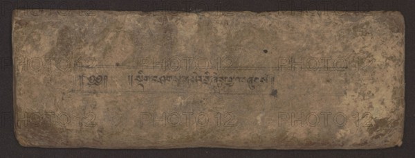 Buddhist Manuscript - Penitential Text Tib. sDig bshags gser gyi zhes bya ba bzhugs+o, unknown author/scribe, Tibetan Buddhist art, Himalayan culture, Book in Tibetan pecha style, manuscript in student's script. Leaf numbering 2–22 verso, first recto, last two unnumbered. Handwritten notes folio 24 recto and verso. 19th century, Tibet, manuscript, width 24.0 cm, height 8.1 cm, A worn rectangular object with rounded corners lying on a dark background, showing an uneven, textured surface with creases and scuffs; the surface displays a palette of brown, tan, beige, and muted gray-green tones with a few darker brown and black spots; faint rectangular border lines and a narrow horizontal band are visible across the central area, and within that band there is a row of dark, short vertical and curved marks; the edges appear slightly darker and more worn than the center, and there are areas of subtle discoloration and blotchy patterns across the entire surface.
