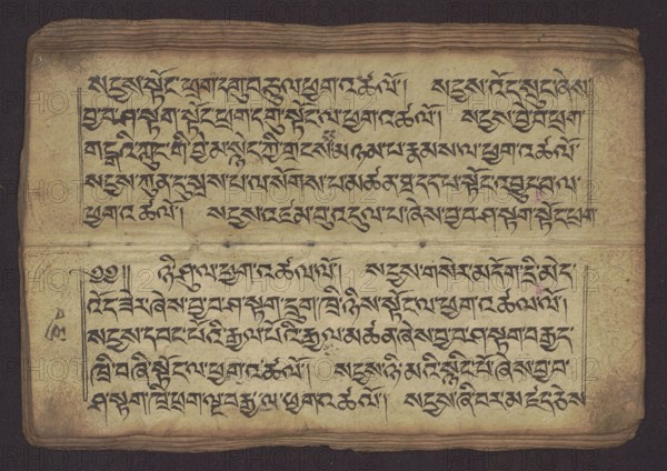 Buddhist Manuscript - Penitential Text Tib. sDig bshags gser gyi zhes bya ba bzhugs+o, unknown author/scribe-copyist, Tibetan Buddhist art, Himalayan culture, Book in Tibetan pecha style, manuscript in student's script. Leaf numbering 2-22 verso, first recto, last two unnumbered. Handwritten notes folio 24 recto and verso. 19th century, Tibet, manuscript, width 24.0 cm, height 8.1 cm, An aged, rectangular sheet with a textured, yellowed surface occupies the image, displaying dense, flowing dark ink strokes arranged in horizontal lines across the page; the ink appears black and contrasts with the warm beige and tan of the paper, which shows darker brown edges and slight discoloration spots; a horizontal fold or seam divides the sheet into upper and lower sections, and the top edge has a stack of layered pages visible with brownish tones; faint purple and pink blotches appear in small areas, and subtle greyish smudges and stains dot parts of the surface; thin, dark framing lines border s...