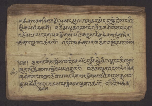 Buddhist Manuscript - Penitential Text Tib. sDig bshags gser gyi zhes bya ba bzhugs+o, unknown author/scribe, Tibetan Buddhist art, Himalayan culture, Book in Tibetan pecha style, manuscript in student's script. Leaf numbering 2-22 verso, first recto, last two unnumbered. Handwritten notes folio 24 recto and verso. 19th century, Tibet, manuscript, width 24.0 cm, height 8.1 cm, A rectangular aged manuscript page lies flat against a dark background, showing a worn, yellowed surface with darker brown edges and horizontal creases near the top and bottom. The page contains several horizontal rows of dense, flowing dark ink script arranged within faint ruled margins, with thicker black strokes forming ornate characters. There are a few small ink smudges and spots on the paper surface and some darker discoloration along the fold lines. The background surrounding the page is deep black, while the manuscript itself shows colors of pale beige, tan, brown, dark brown, and black.