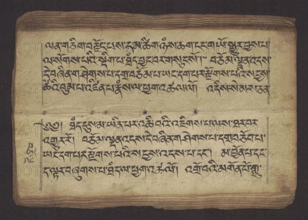 Buddhist manuscript — Penitential Text Tib. sDig bshags gser gyi zhes bya ba bzhugs+o, unknown creator / scribe-copyist, Tibetan Buddhist art, Himalayan culture. Book in Tibetan pecha style, manuscript in student's script. Leaf numbering 2–22 verso, first recto, last two unnumbered. Handwritten notes folio 24 recto and verso. 19th century, Tibet. Manuscript; width 24.0 cm, height 8.1 cm., An open aged book page with a worn cream-colored paper showing dark brown edges and layered, slightly darker brown pages at top and bottom; the page contains a group of black handwritten script arranged in two horizontal blocks separated by a faint horizontal crease and a few small dark spots; thin vertical margin lines frame the text on both sides and a few ink marks appear near the left margin; the background around the book is a deep dark brown.