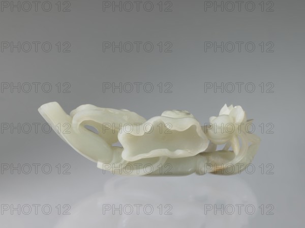 Lotus branch - decoration; maker, purchase provenance; Chinese art; Chinese culture; Qing dynasty 1644–1911; lotuses, flowers; 19th century, China; decoration; height 5.1 cm, width 14.0 cm, depth 3.3 cm., A carved ornamental object resembling a flowing organic form with curved, undulating edges and petal-like shapes, featuring a lotus-like blossom at one end and layered, scalloped surfaces along its length, all rendered in a smooth, translucent pale material with highlights and subtle glossy reflections; the predominant colors are off-white and creamy pale green with a few areas showing light beige and faint amber tones, set against a neutral gray background with soft reflections beneath the object.