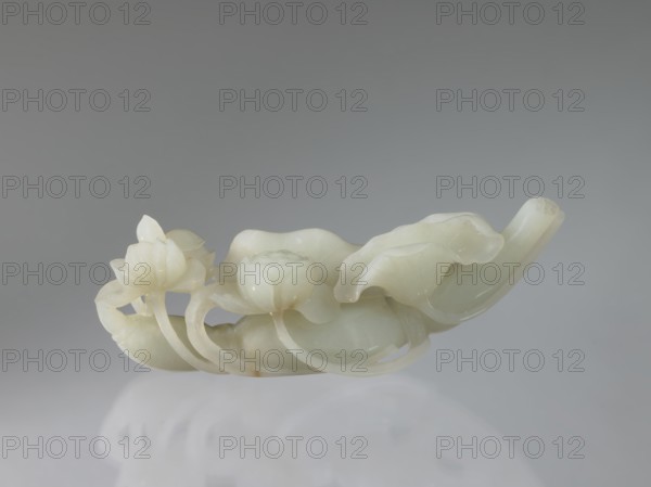 Lotus branch — decoration; maker, purchase provenance; Chinese art; Chinese culture; Qing dynasty 1644–1911; lotuses, flowers; 19th century; China; decoration; height 5.1 cm, width 14.0 cm, depth 3.3 cm., A smooth carved object resembling a group of lotus flowers and leaves sits against a neutral gray background, the carving showing rounded petals, curved stems, and layered leaves with gentle undulations; the material appears translucent and pale, showing shades of off-white, cream, and very light green with subtle glossy surfaces and soft reflections, and a faint shadow and reflection appear beneath the piece on the surface it rests on.