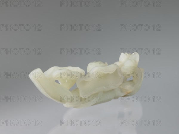 Lotus branch — decoration; maker, purchase provenance noted; Rubiec-Masalski; Fyodor Vasilyevich 1865–c.1920; Tulisow, Jerzy 1943– ; Chinese art; Chinese culture; Qing dynasty 1644–1911; lotuses, flowers; 19th century; China; decoration; height 5.1 cm, width 14.0 cm, depth 3.3 cm, A pale, translucent carved object with smooth, curving forms and undulating edges sits against a soft gray background; the piece shows a few layered, petal-like shapes and rounded bulbous elements, with glossy surfaces and subtle variations in color including off-white, cream, and hints of very light green, resting on a reflective surface that casts a faint, blurred reflection.