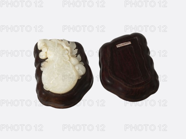 Box with a decorated jade plaque;, container/box; Qing style, 19th century Qing 1644–1911; Chinese; gourds; box; height 4.8 cm, width 9.0 cm, depth 6.8 cm., A pair of carved objects resting on a pale background, each set into a dark wooden base. One object is a light, creamy white carved piece with smooth, rounded, and undulating organic shapes and subtle translucent areas, sitting on a deep brown wood base with a gently scalloped outline. The other is a dark brown wooden piece with a similarly shaped scalloped edge and a carved recessed area, showing rich wood grain in darker and lighter brown tones. Overall the visible colors include creamy white, deep brown, dark brown, and lighter brown.