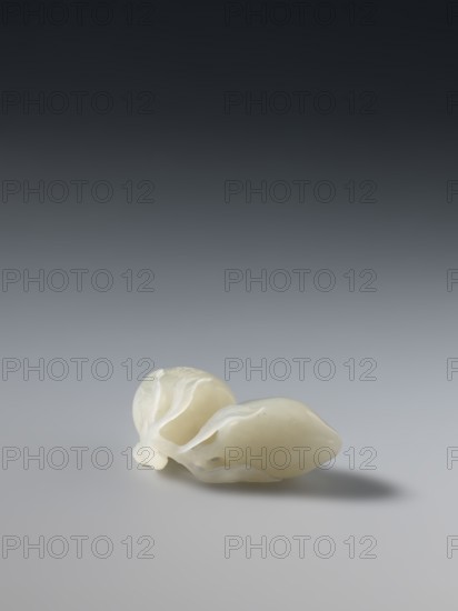 Paperweight — peaches; maker, Chinese; Qing dynasty, Qianlong period 1736–1795; painted Qianlong style; materials: paperweight; dimensions: height 5.7 cm, width 3.4 cm; iconography: peaches., A small pale object with a smooth, slightly glossy surface rests on a flat surface, showing a creamy off-white color with subtle translucent white layers or thin petal-like edges; the background transitions from dark gray at the top to light gray near the bottom, and a soft shadow appears beside the object.