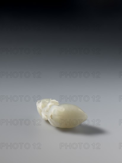 Paperweight — peaches; maker, Chinese; Chinese art; peaches iconography; Qianlong 1736–1795; Qianlong style; Qing 1644–1911; date: 1736–1795; medium: paperweight; dimensions: height 5.7 cm, width 3.4 cm., A smooth pale object with an off-white, creamy color rests on a neutral gray surface, casting a soft shadow; the object has an elongated, rounded form with a glossy finish and a section showing intricate carved or molded details and small curved protrusions, and the background transitions from light gray near the surface to dark gray and nearly black toward the top.